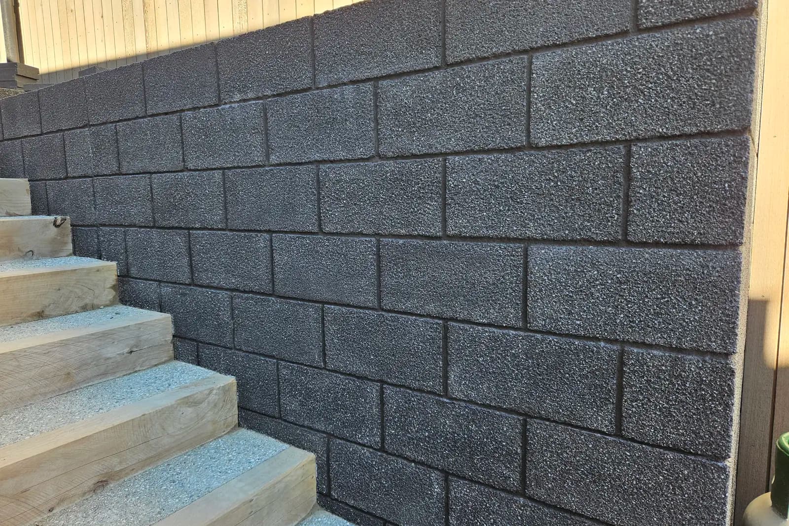 Charcoal split-face concrete block retaining wall sealed with a breathable masonry sealer, timber steps alongside, Queenstown