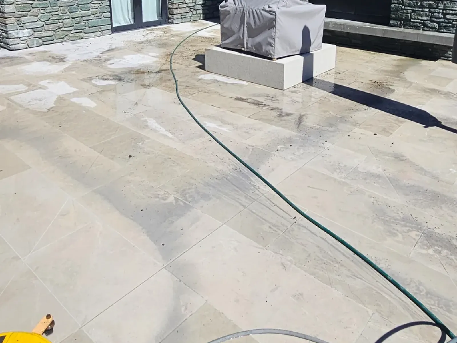 Limestone patio mid-clean with hose laid out, schist barbecue area in the background, Wanaka